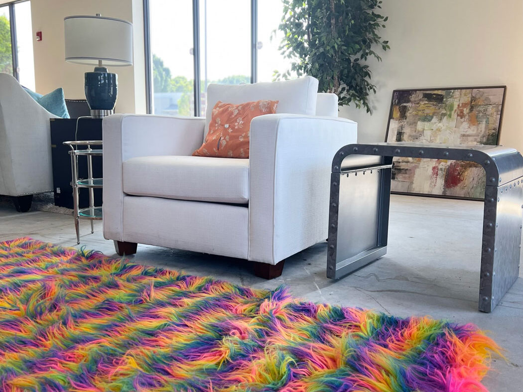 White small love seat couch in front of a rainbow fluffy carpet.