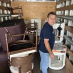 a man in a blue shirt and blue jeans standing inside of a truck filled with furniture