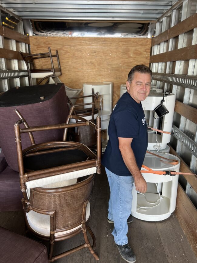 a man in a blue shirt and blue jeans standing inside of a truck filled with furniture