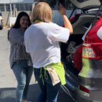 a woman in a white shirt helping another woman load items into the back of an SUV