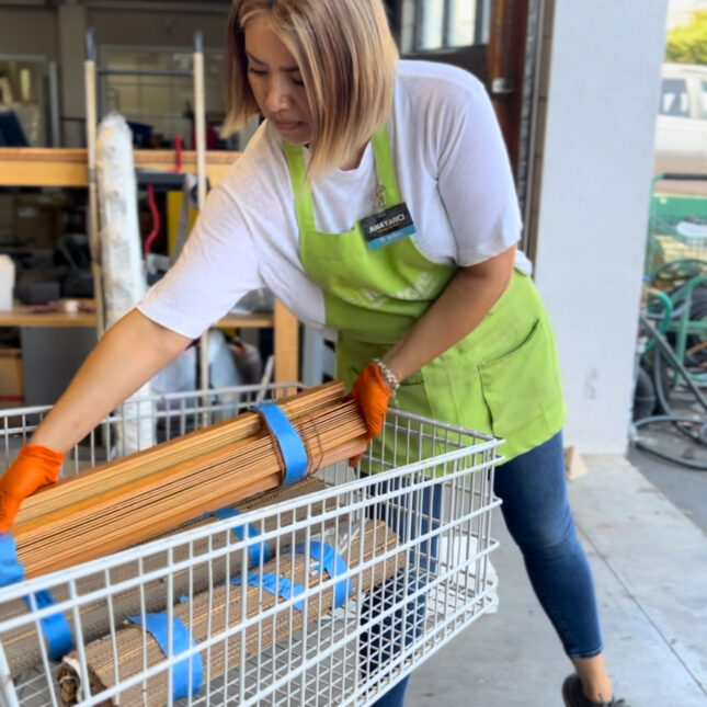 a woman in a white shirt and green apron loading wood items into a cart