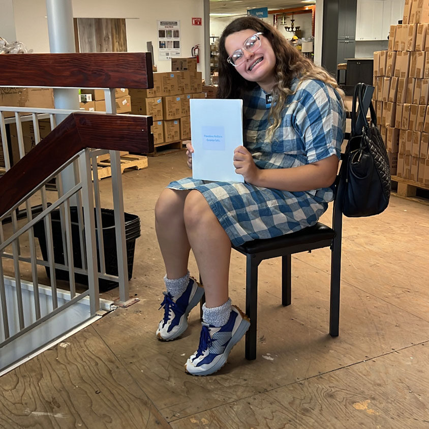 Young girl volunteer smiling on a chair holding a book.