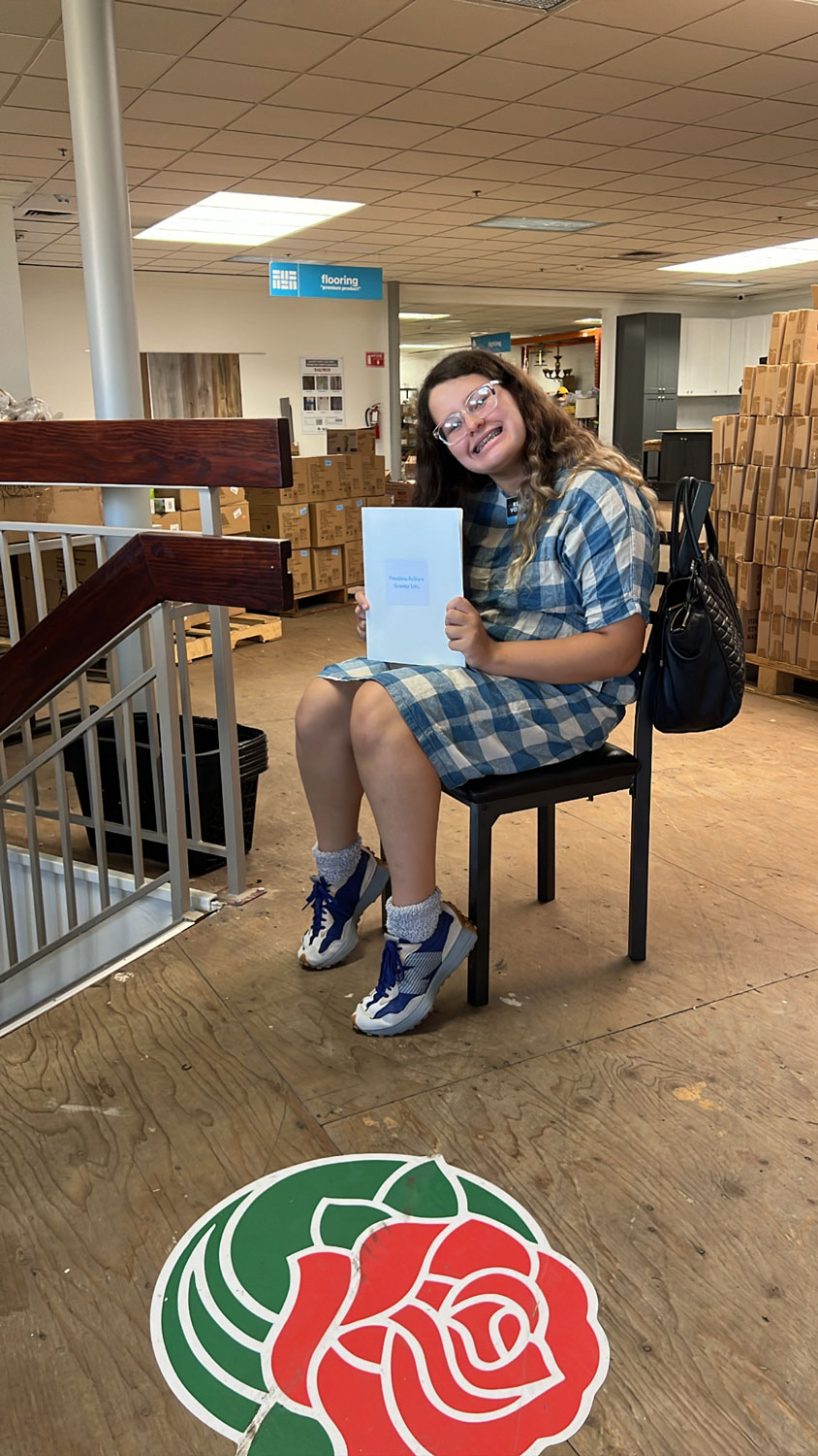 Young girl volunteer smiling on a chair holding a book.